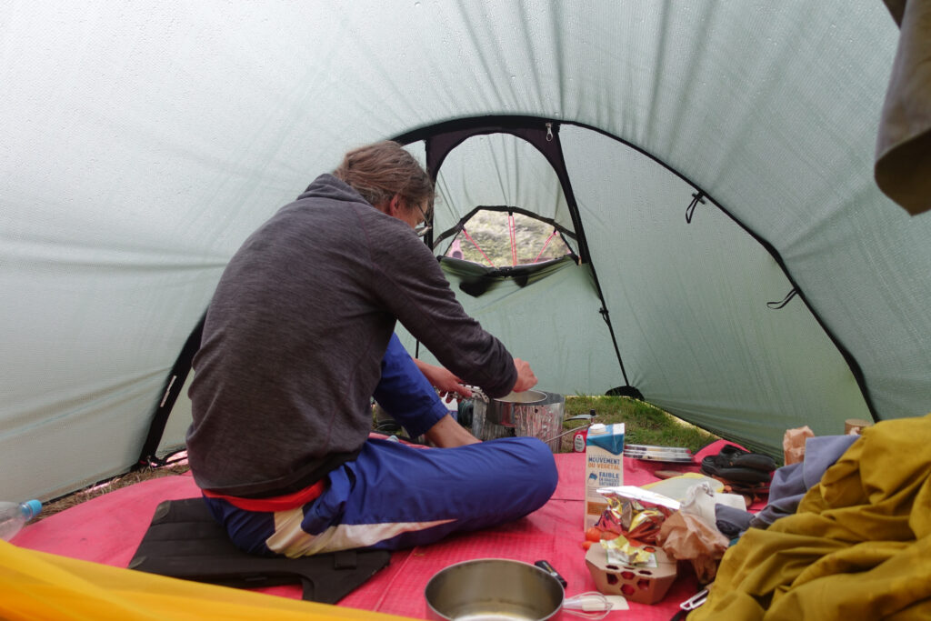 Lo sitzend beim Kochen im Vorzelt