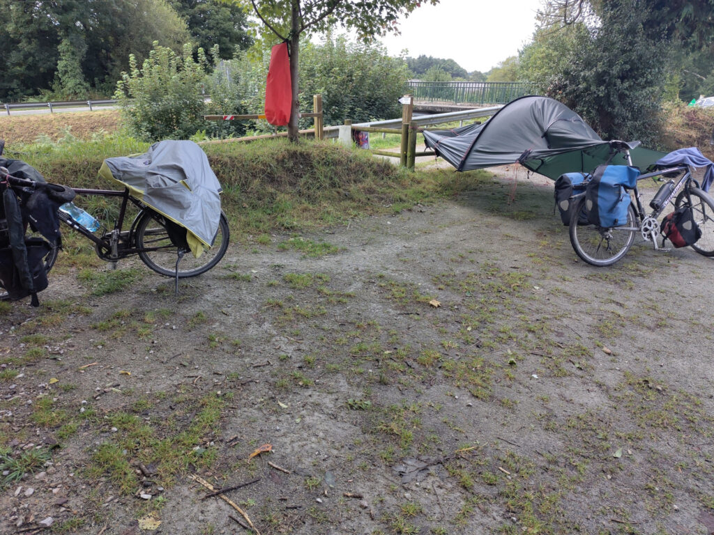 Jacken, Handtücher und Sesack sind an Velos und Bäumen aufgehängt. Das Aussenzelt an einem Zaun und einem Velo befestigt wiegt sich im Wind.