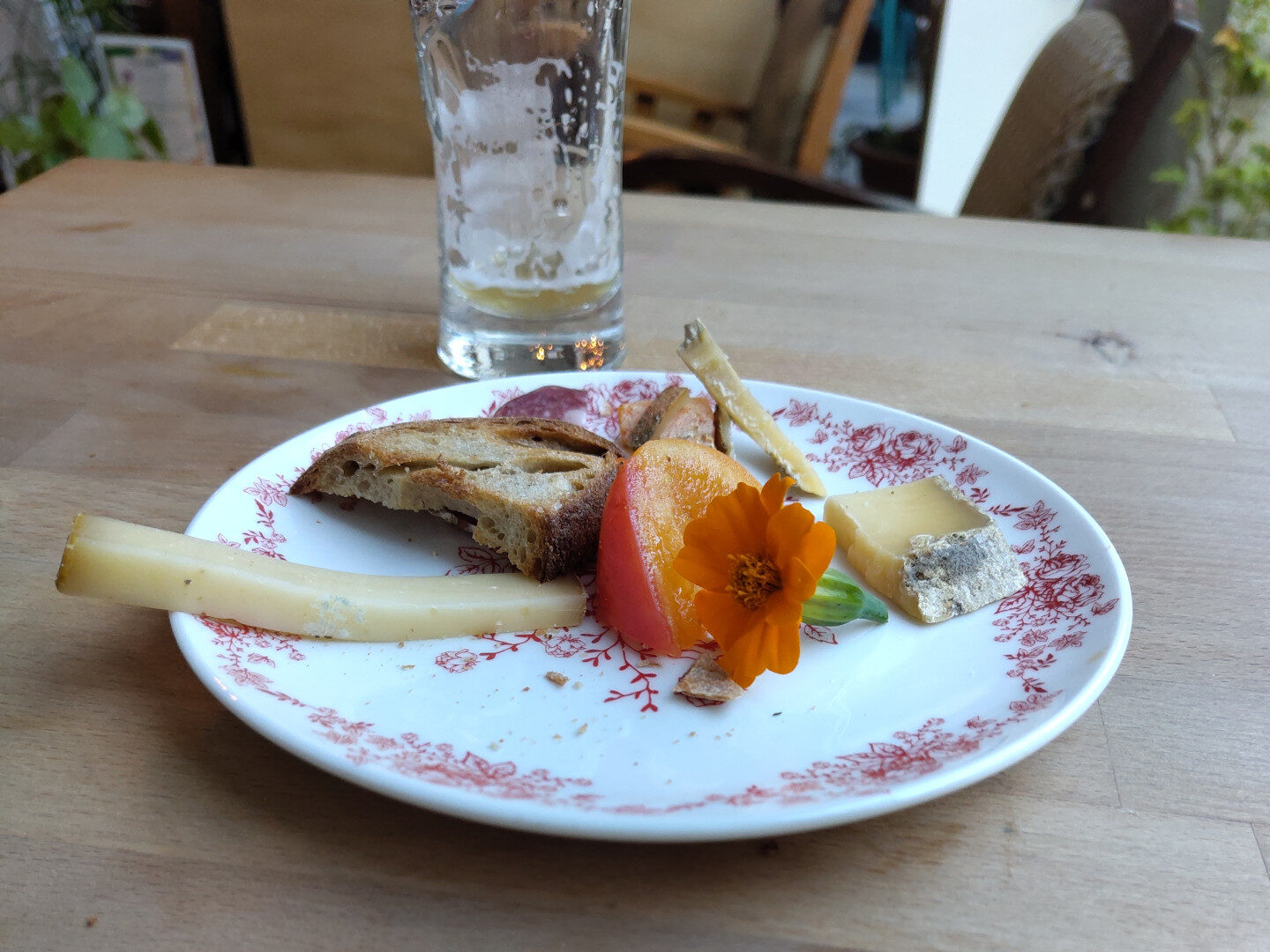 Leeres Bierglass und Teller mit Brot, Käse, einem Tomatenschnitz und einer Blumenblüte.