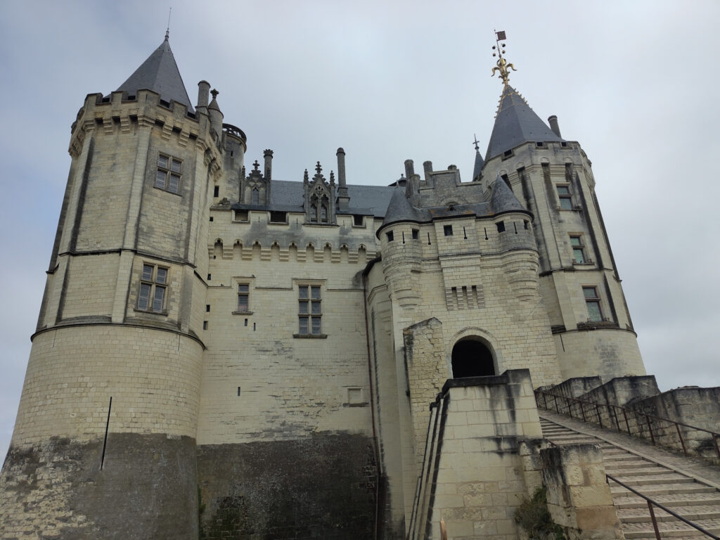 Ein Schloss aus Stein mit zwei markanten grösseren Türmen rechts und links. Dazwischen viele Erker, Fenster und Verzierungen. Etwa in der Mitte befindet sich das grosse Tor.