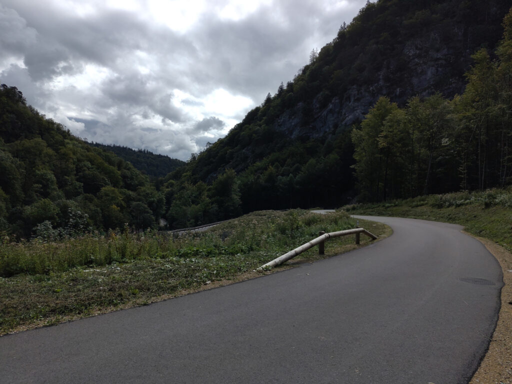 Neugeteerte kurvige Strasse. Der Strassenrand ist bewachsen. Im Hintergrund geht es runter in Schlucht. Rechts und links Felsen mit Bäumen und Sträucher bewachsen.