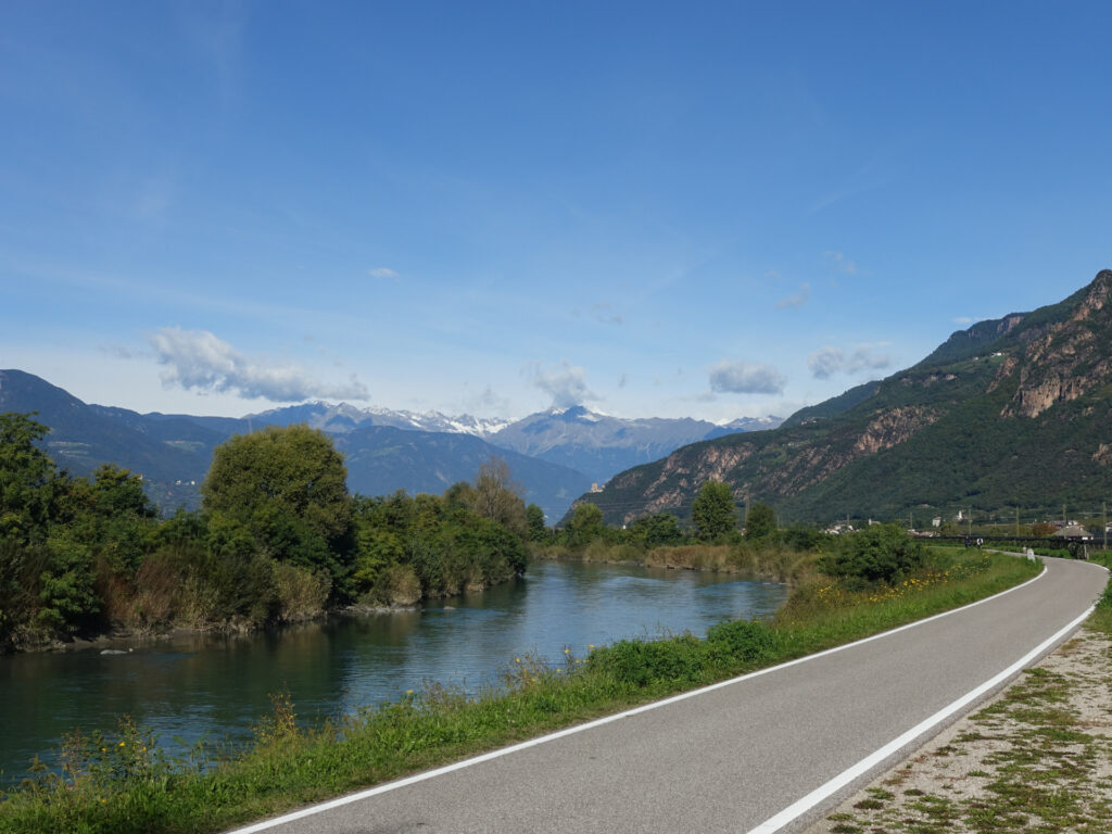 Von der asphaltierten Strasse geht der Blick über den Fluss Etsch die Berge.
