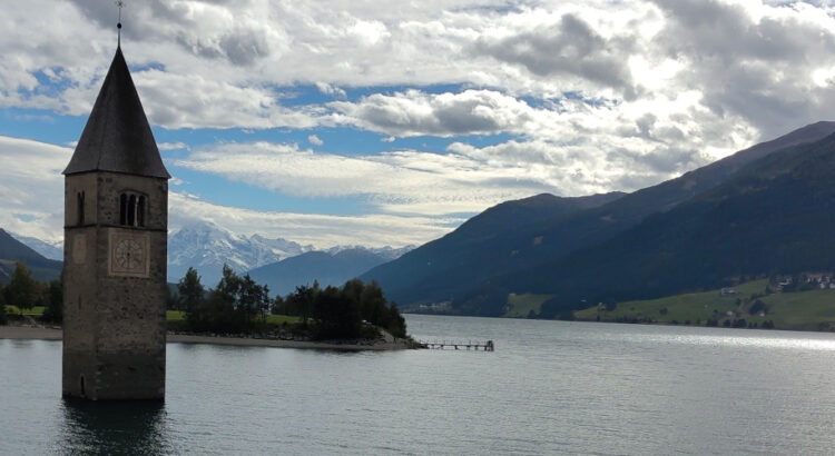 Kirchturm im Stausee. Im Hintergrund die Flanken der umgebenden Hügel und blauer Himmel mit weissen Wolken.