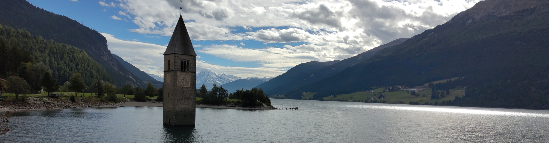Kirchturm im Stausee. Im Hintergrund die Flanken der umgebenden Hügel und blauer Himmel mit weissen Wolken.